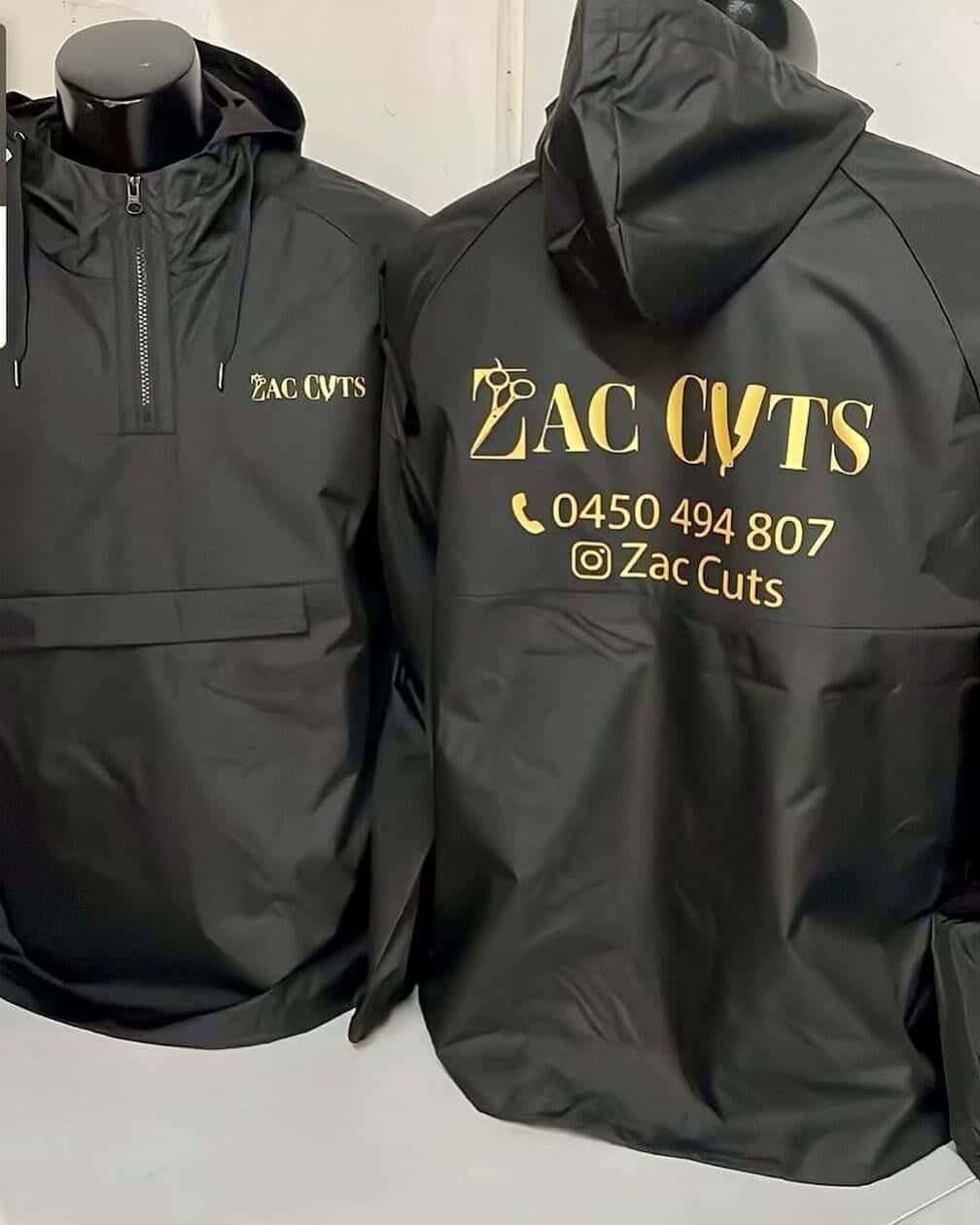Black Zac's Cuts barber shop jackets with the gold shop logo on the chest and the logo and phone number on the back, made by South West Apparel