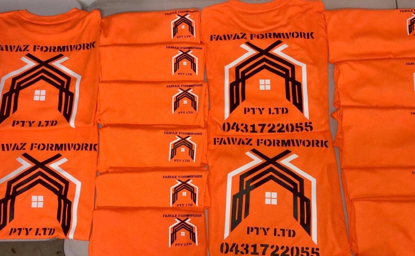 A stack of bright orange Fawaz Formwork tees with a large black company logo and phone number on the back