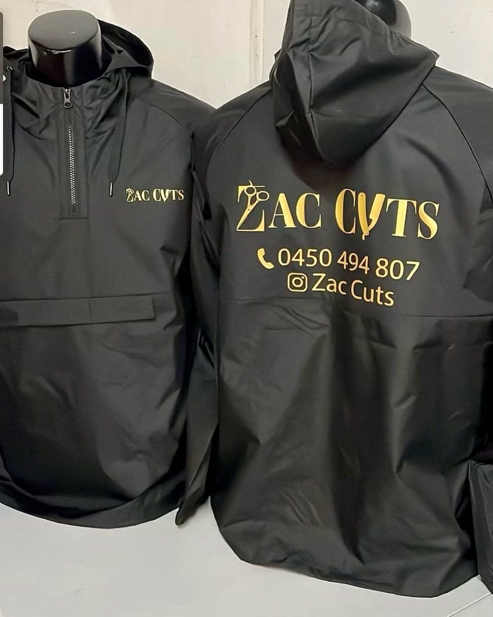 Black Zac's Cuts hooded jackets, one showing the gold script logo and phone number across the back
